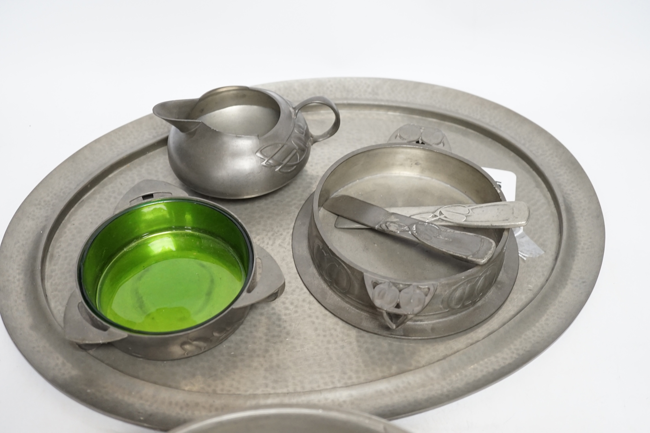 Seven items of pewter, including a Liberty Tudric tray, 45.5cm width, an Archibald Knox jug, a large Tudric bowl, 27cm diameter, a dish with glass liner, another dish and two paper knifes